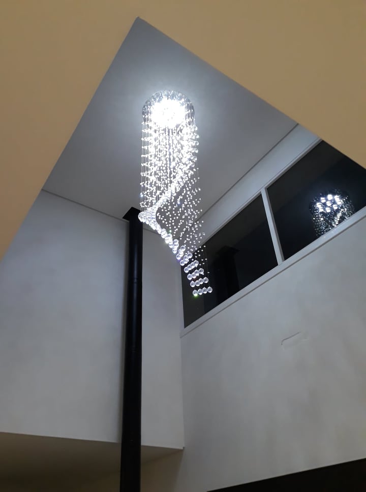Lustre de cristal design S Rico instalado em sala com pé direito duplo, destacando cristais K9 legítimos da Linha Kria, ideal para ambientes sofisticados.